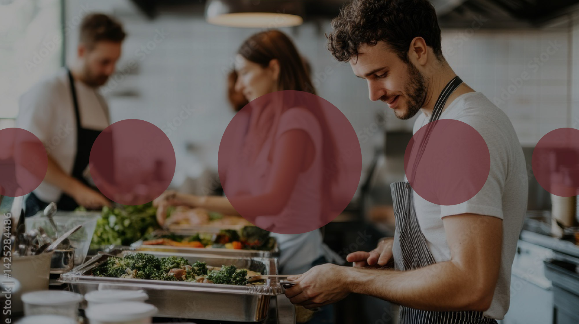 Mehrere Personen bereiten in einer Küche Speisen zu; über dem Bild liegen halbtransparente rote Kreise als grafisches Gestaltungselement.