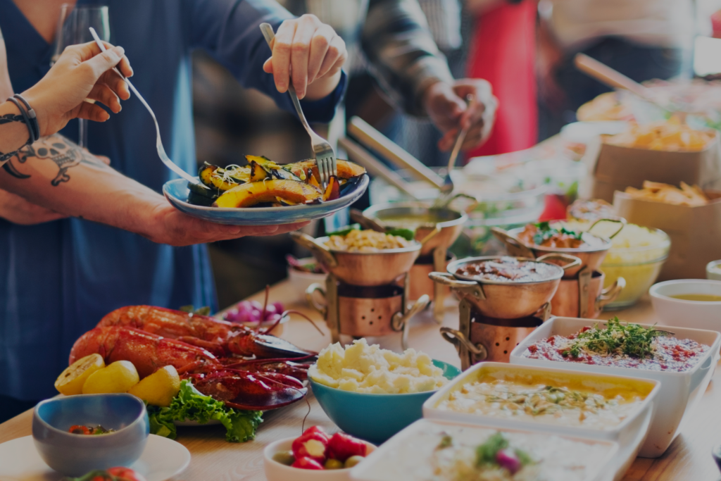 Mehrere Personen bedienen sich an einem reichhaltigen Buffet mit warmen Speisen, Salaten und Meeresfrüchten.