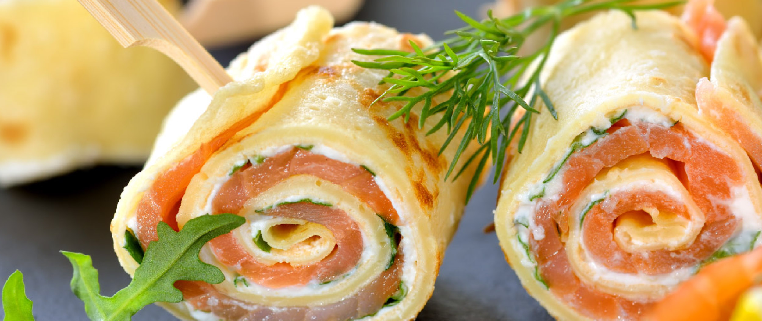 Nahaufnahme von herzhaft gefüllten Crêpe-Röllchen mit Lachs, Frischkäse und Kräutern, garniert mit Dill und Rucola.