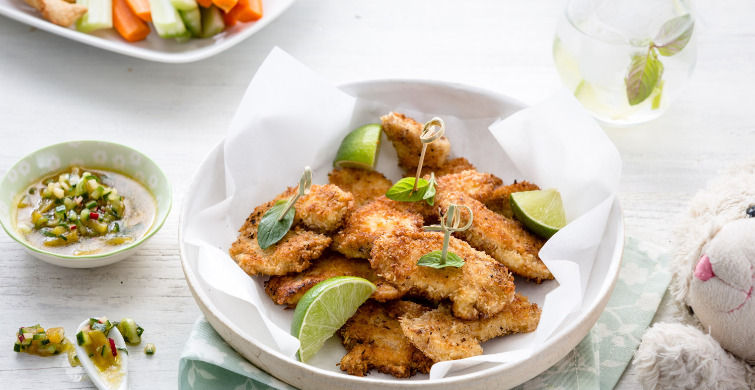 Teller mit panierten Hähnchenstücken, Limettenspalten und Dip.
