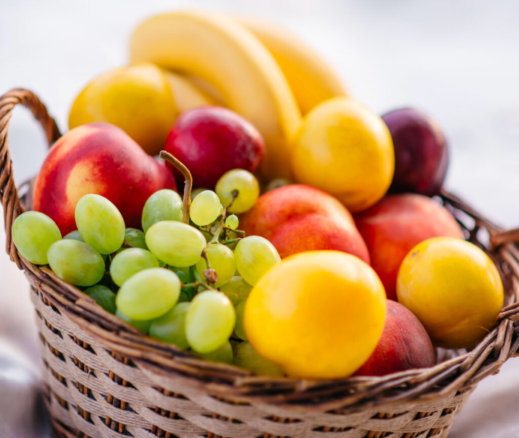 Obstkorb mit grünen Trauben, roten Nektarinen und gelben Pflaumen.